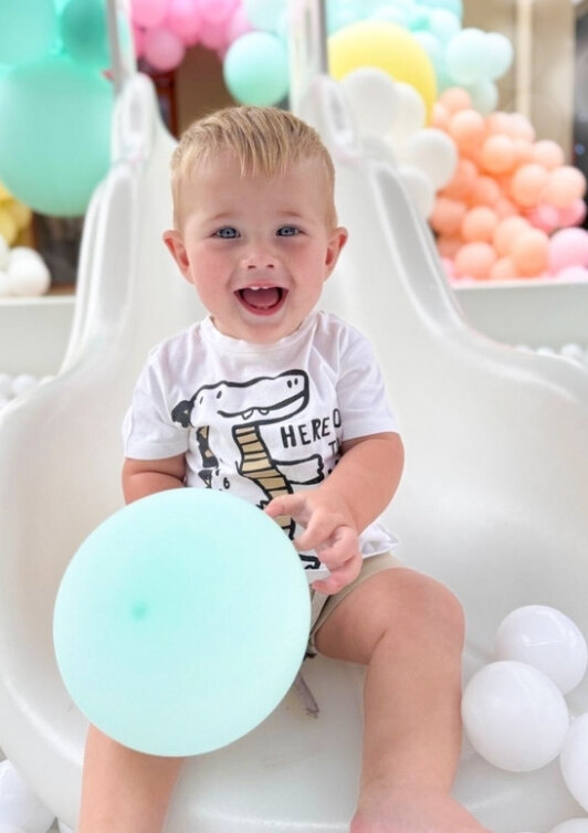 Smiling toddler holding a mint balloon on a white soft play slide